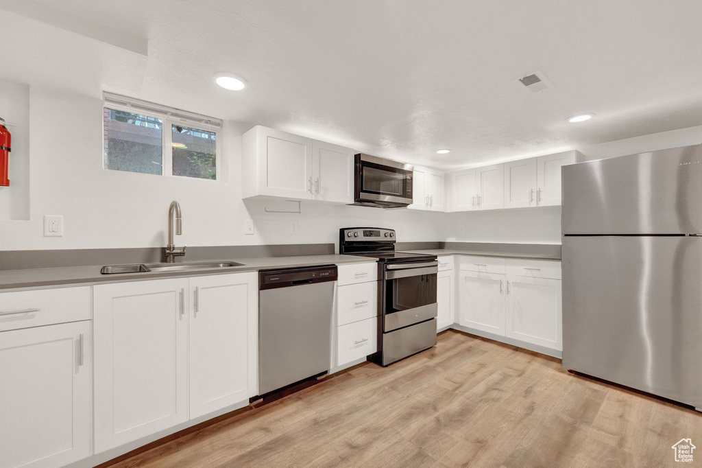Kitchen with appliances with stainless steel finishes, sink, white cabinets, and light wood-type flooring