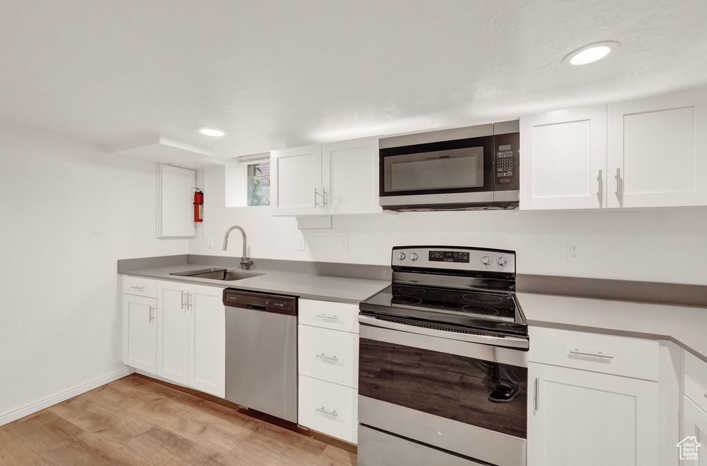 Kitchen with sink, light hardwood / wood-style flooring, white cabinets, and appliances with stainless steel finishes
