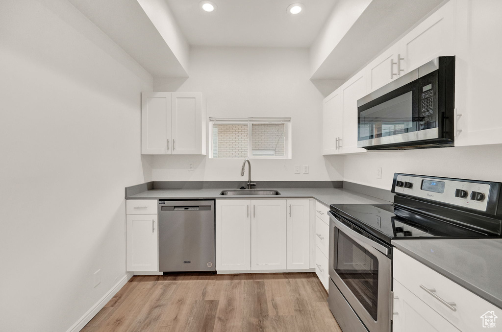 Kitchen with sink, white cabinets, light wood-type flooring, and stainless steel appliances