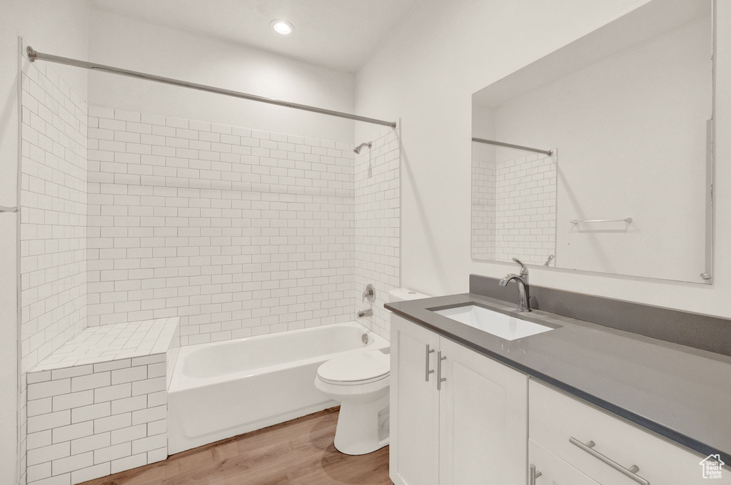 Full bathroom with tiled shower / bath combo, vanity, toilet, and wood-type flooring