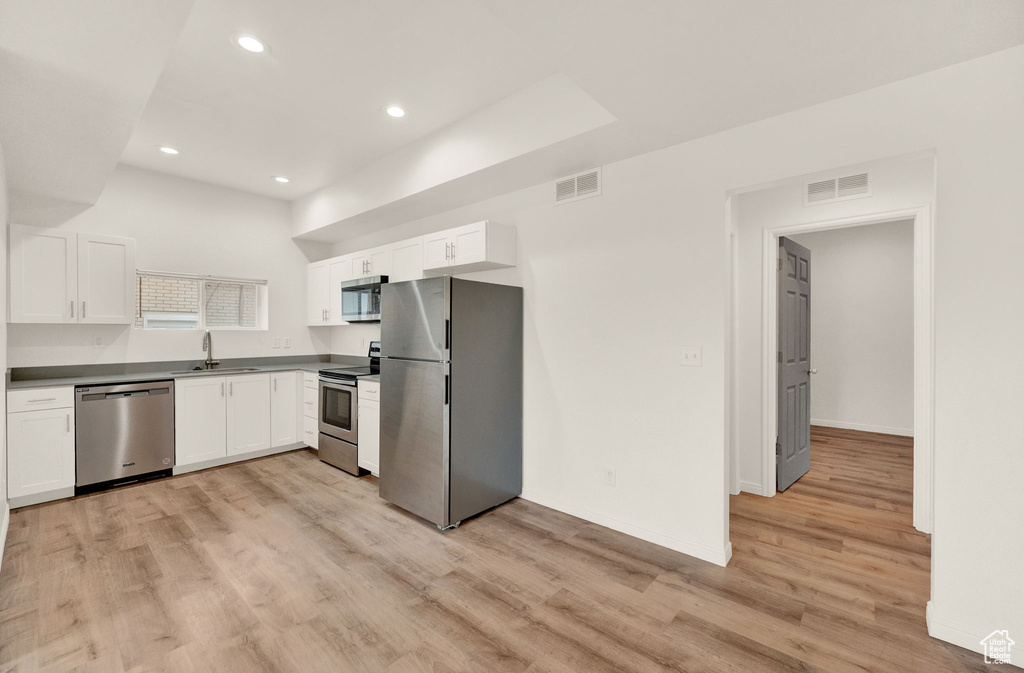 Kitchen with stainless steel appliances, light hardwood / wood-style flooring, white cabinets, and sink