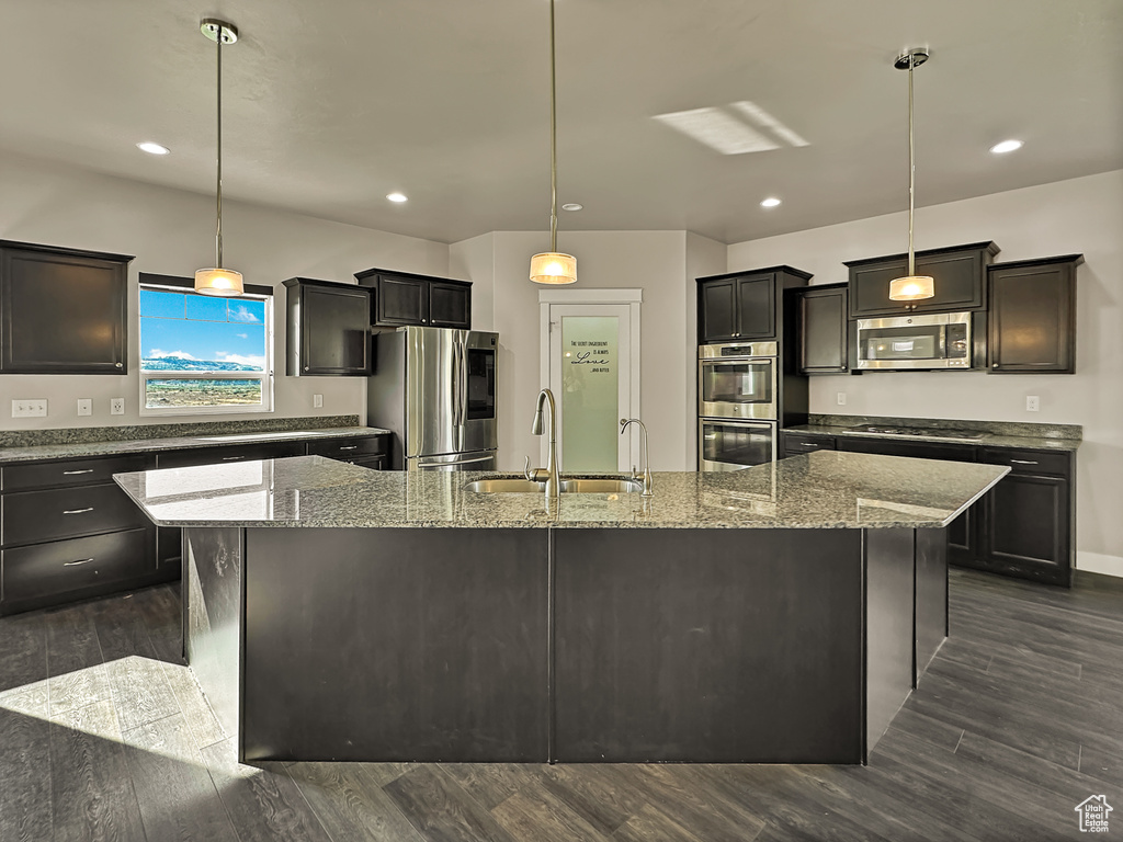 Kitchen featuring a kitchen island with sink, appliances with stainless steel finishes, dark hardwood / wood-style flooring, and hanging light fixtures