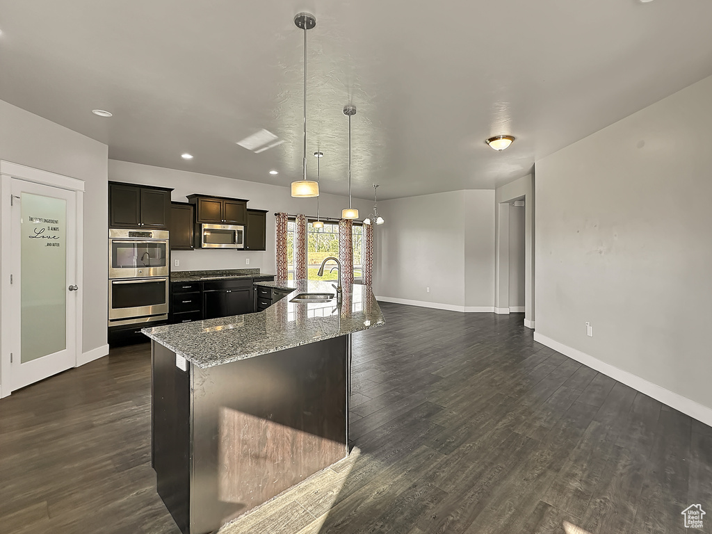 Kitchen with dark hardwood / wood-style flooring, an island with sink, stainless steel appliances, and hanging light fixtures