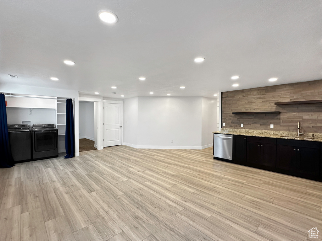 Kitchen with light hardwood / wood-style floors, dishwasher, light stone countertops, washing machine and dryer, and sink