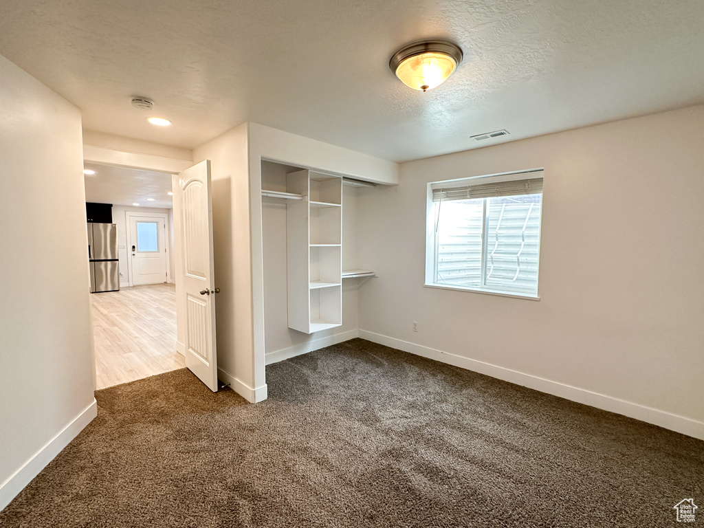 Unfurnished bedroom featuring stainless steel fridge, a closet, and carpet