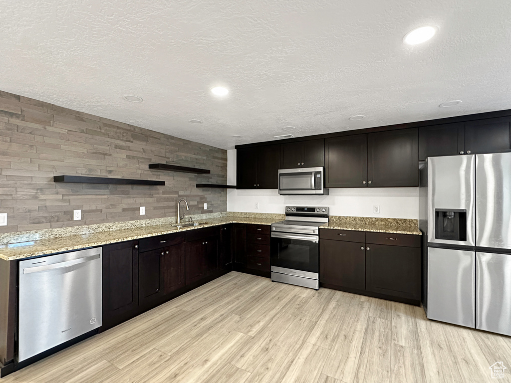 Kitchen featuring light stone countertops, stainless steel appliances, light wood-type flooring, a textured ceiling, and sink