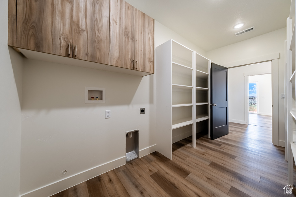 Washroom with hookup for a washing machine, wood-type flooring, hookup for an electric dryer, and cabinets