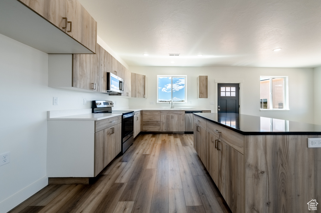 Kitchen with a kitchen island, light brown cabinetry, wood-type flooring, appliances with stainless steel finishes, and sink