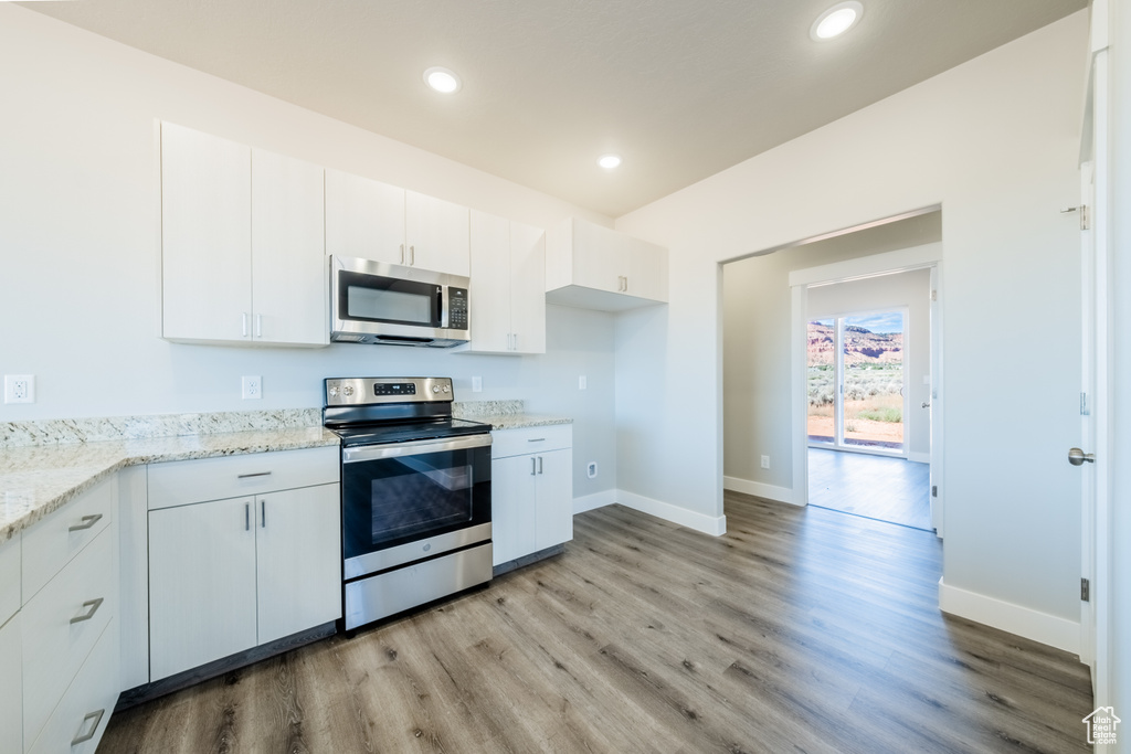 Kitchen featuring light stone counters, light hardwood / wood-style floors, stainless steel appliances, and white cabinets