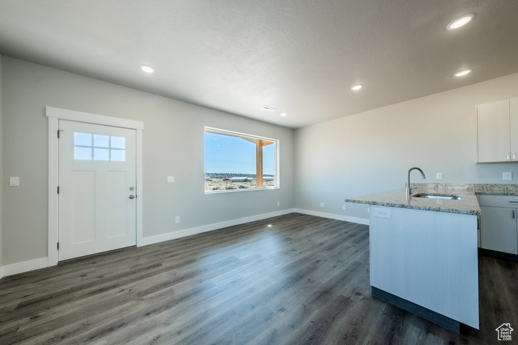 Kitchen featuring light stone counters, dark wood-type flooring, sink, an island with sink, and white cabinetry