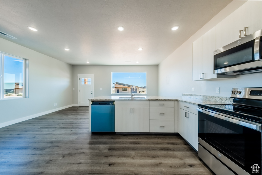 Kitchen with kitchen peninsula, white cabinetry, dark wood-type flooring, and stainless steel appliances