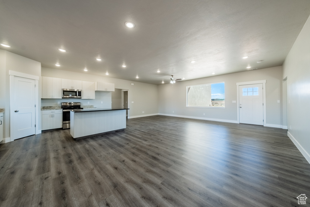 Interior space with a kitchen island with sink, dark hardwood / wood-style flooring, stainless steel appliances, and white cabinets