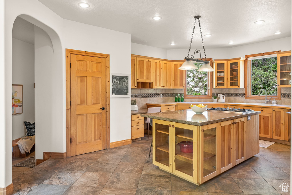 Kitchen with a center island, hanging light fixtures, tile floors, sink, and tasteful backsplash