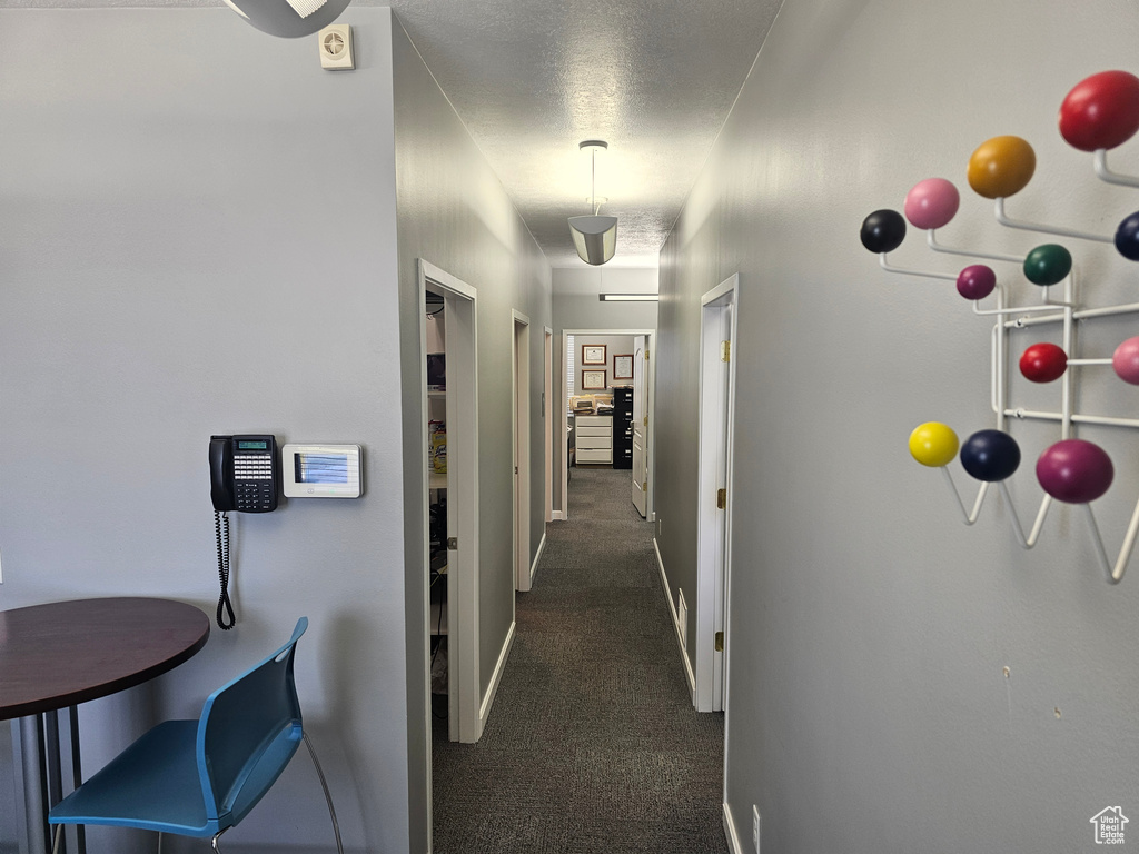 Hall with a textured ceiling and dark colored carpet