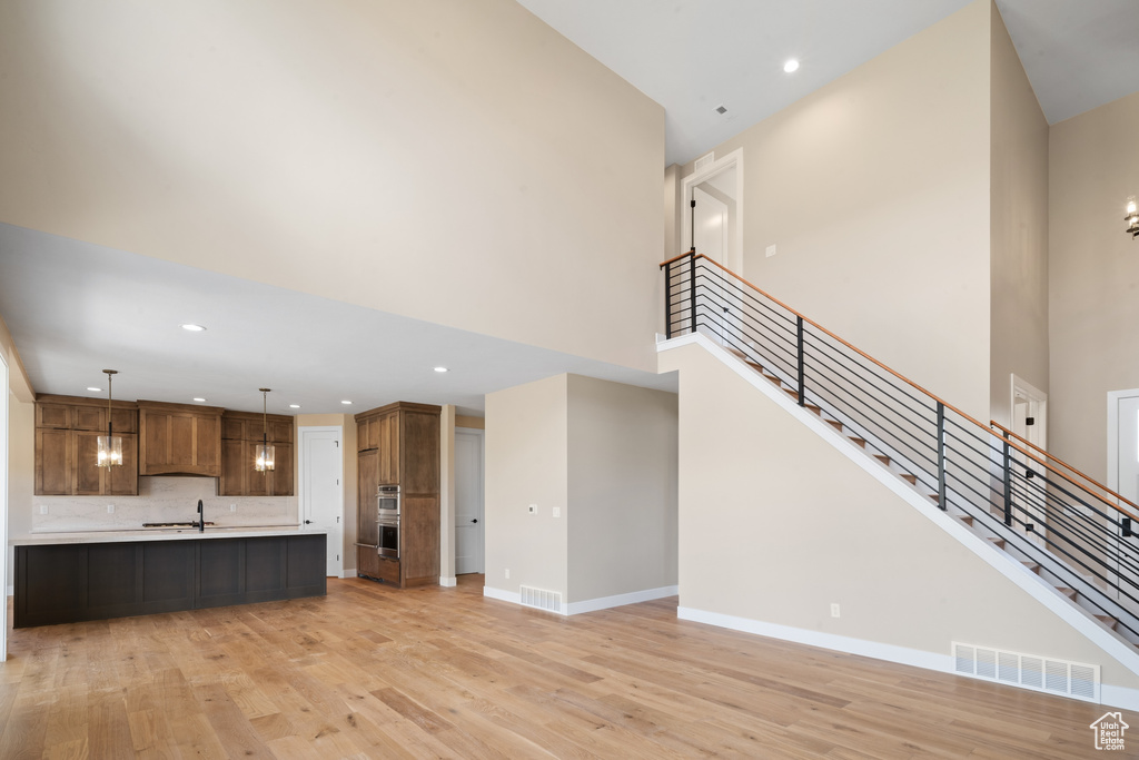 Unfurnished living room featuring sink, a high ceiling, and light hardwood / wood-style flooring