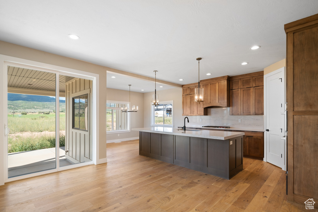 Kitchen featuring light hardwood / wood-style flooring, backsplash, pendant lighting, a kitchen island with sink, and sink