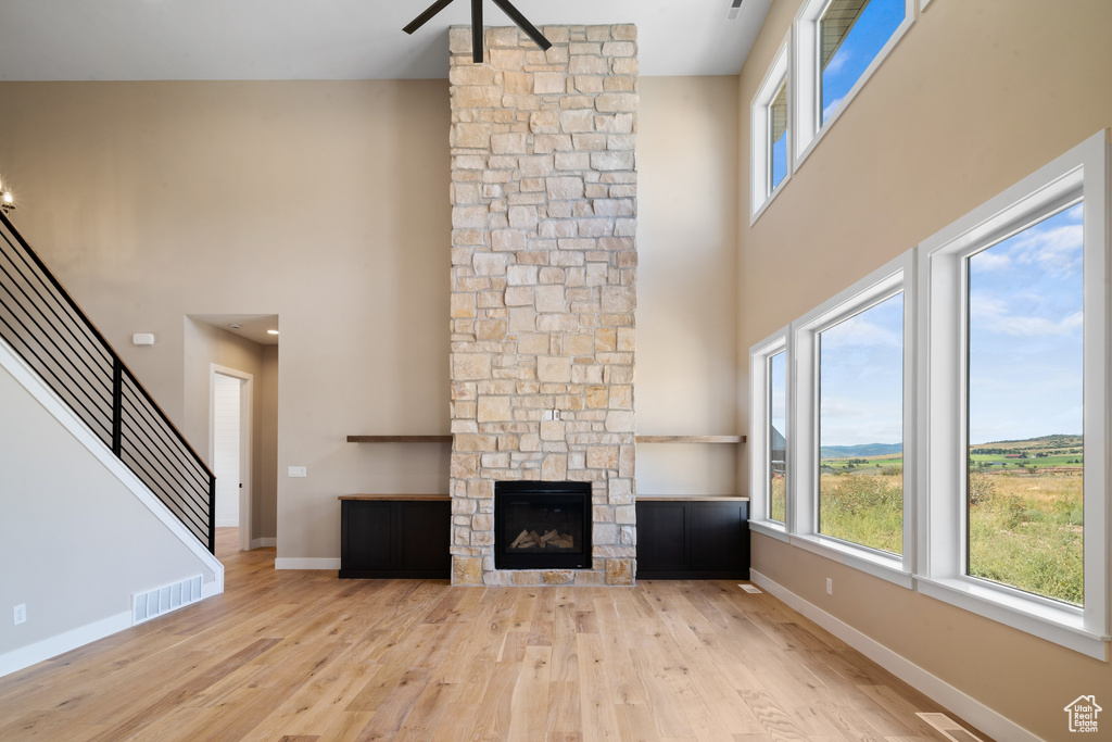 Unfurnished living room with light wood-type flooring, a high ceiling, and a stone fireplace