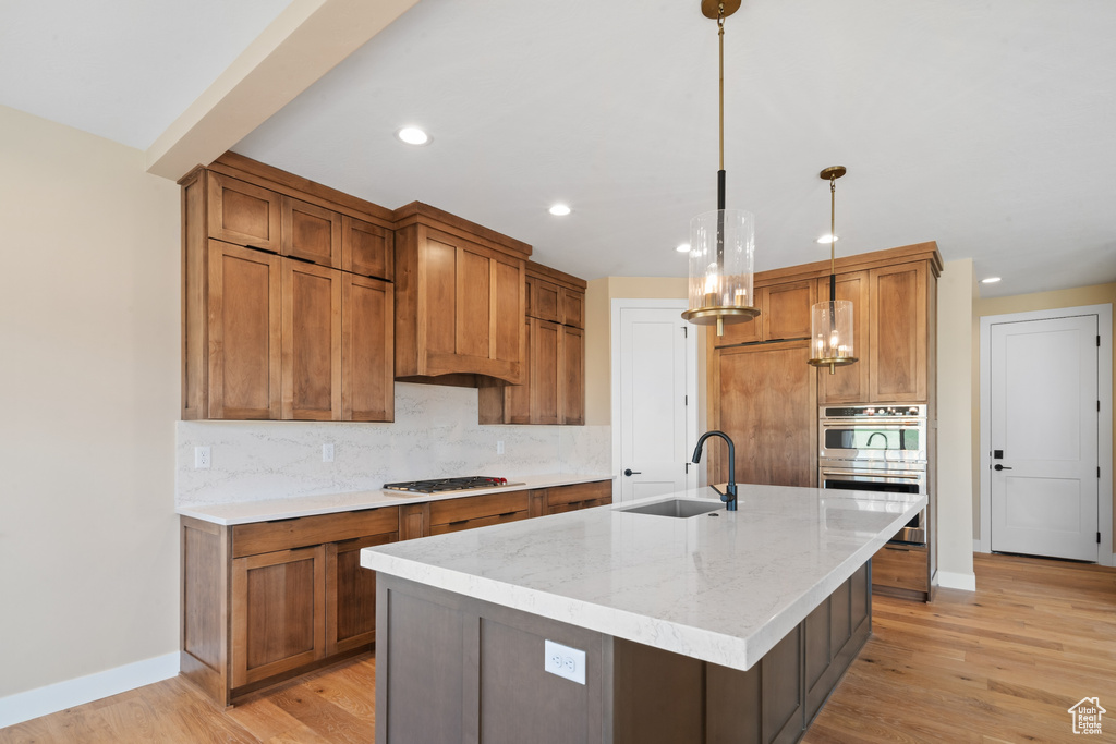 Kitchen with light wood-type flooring, black gas cooktop, sink, and a kitchen island with sink