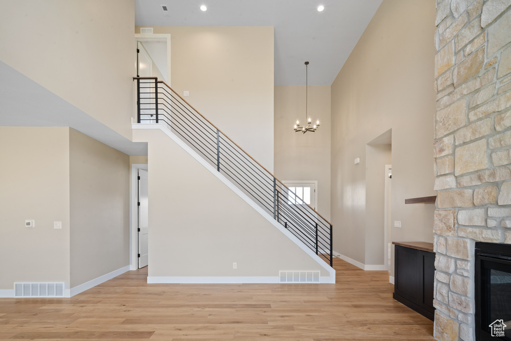 Stairs with a notable chandelier, hardwood / wood-style floors, a stone fireplace, and a towering ceiling