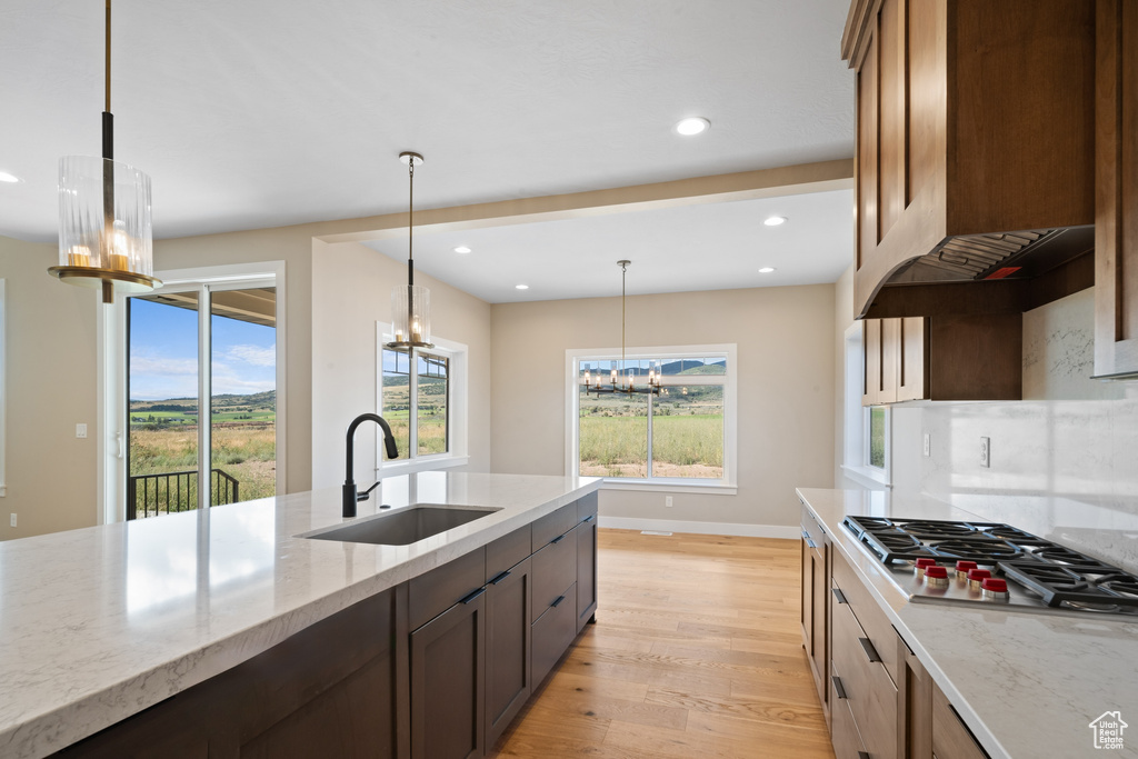 Kitchen featuring light wood-type flooring, stainless steel gas stovetop, light stone counters, sink, and an inviting chandelier