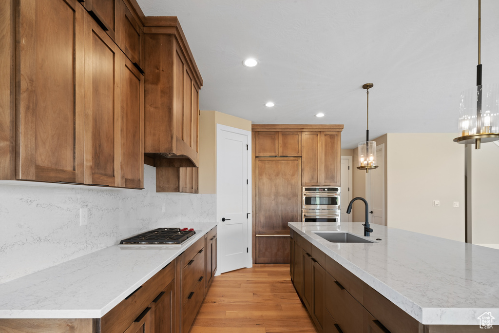 Kitchen with stainless steel appliances, light hardwood / wood-style floors, sink, a center island with sink, and pendant lighting