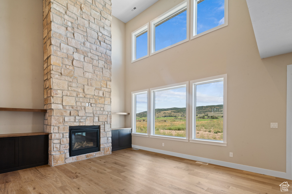 Unfurnished living room with a fireplace, light wood-type flooring, and a high ceiling