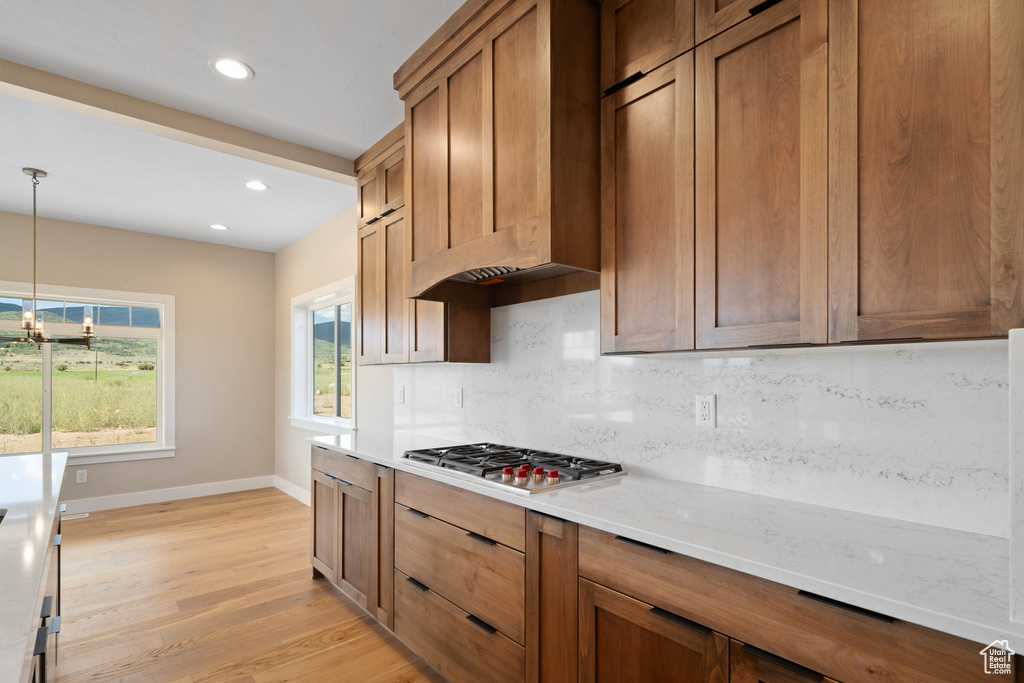 Kitchen with light wood-type flooring, tasteful backsplash, hanging light fixtures, stainless steel gas stovetop, and custom exhaust hood