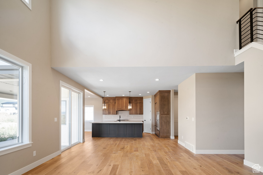 Unfurnished living room featuring a wealth of natural light, light hardwood / wood-style floors, a towering ceiling, and sink