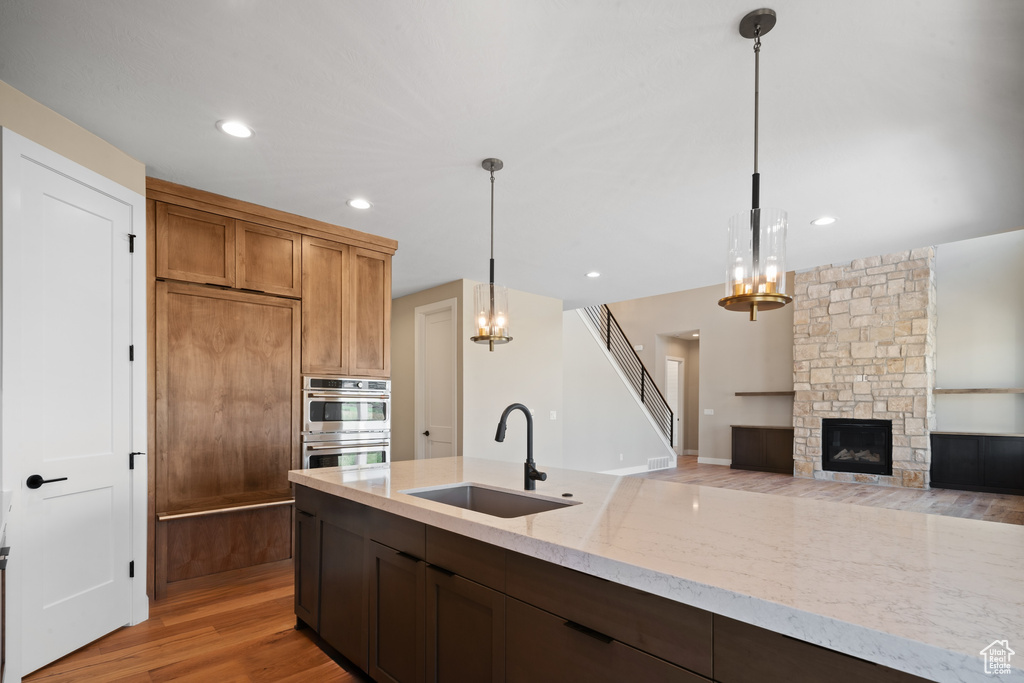 Kitchen with light wood-type flooring, pendant lighting, stainless steel double oven, a stone fireplace, and sink