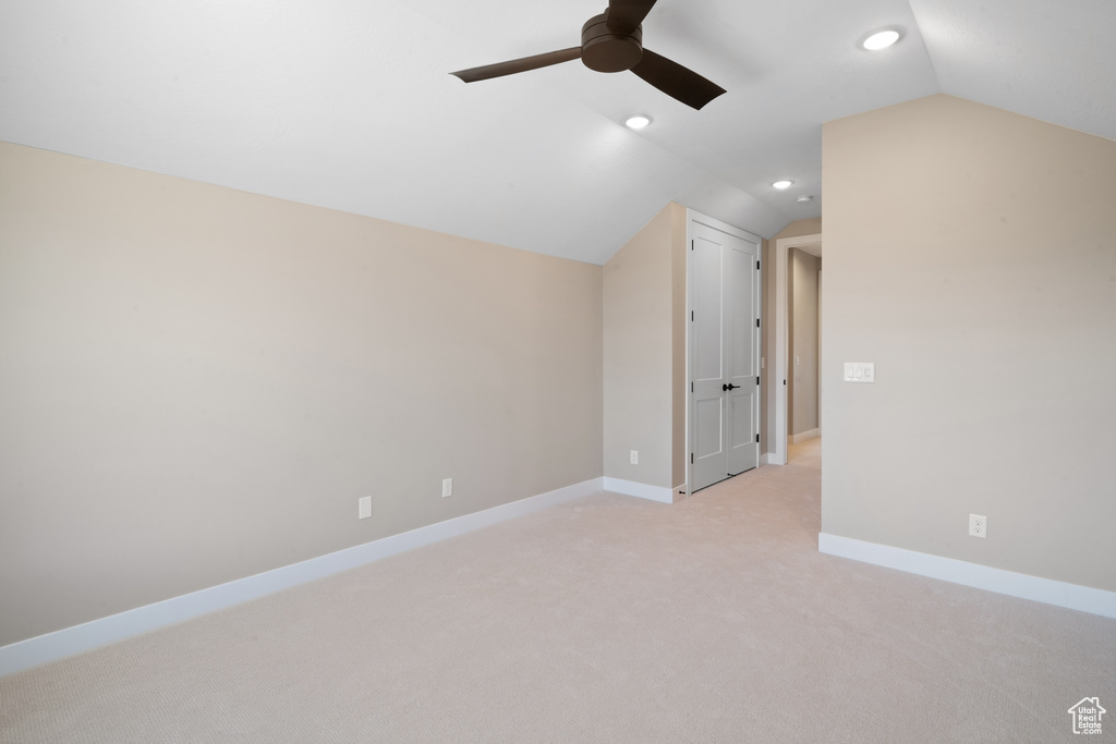 Carpeted spare room featuring ceiling fan and vaulted ceiling