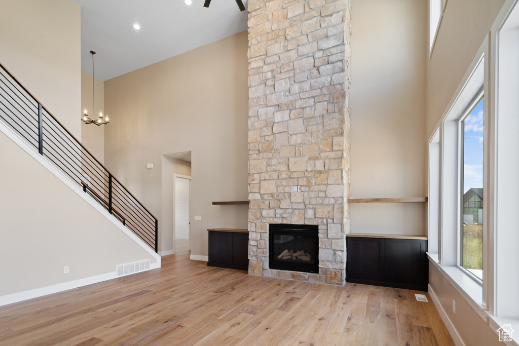 Unfurnished living room featuring light hardwood / wood-style floors, a chandelier, a stone fireplace, and a towering ceiling