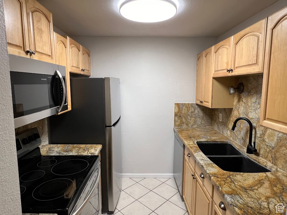 Kitchen with tasteful backsplash, stainless steel appliances, light stone counters, light tile floors, and sink