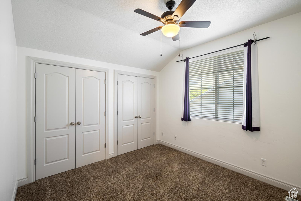 Unfurnished bedroom featuring carpet flooring, two closets, ceiling fan, and lofted ceiling