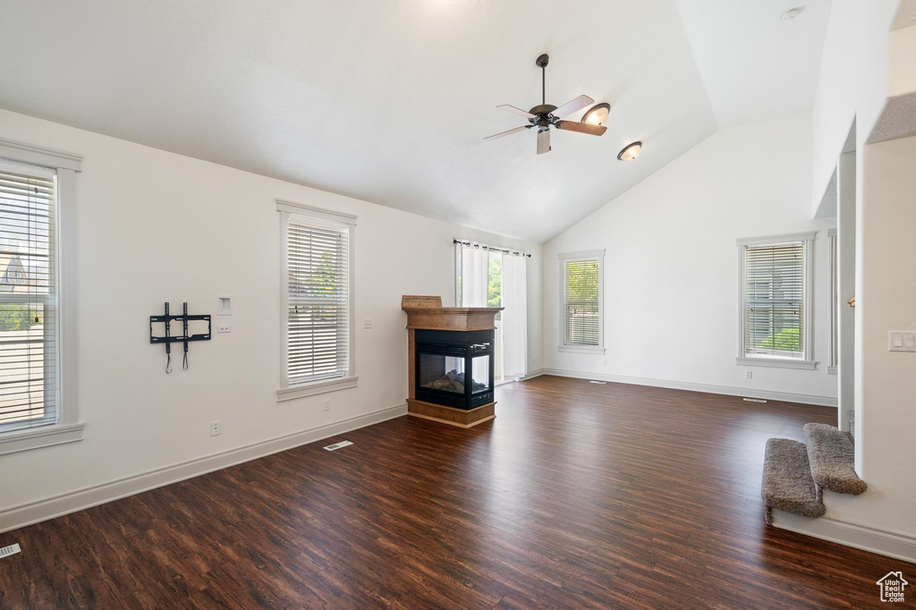 Unfurnished living room with a multi sided fireplace, ceiling fan, high vaulted ceiling, and dark wood-type flooring