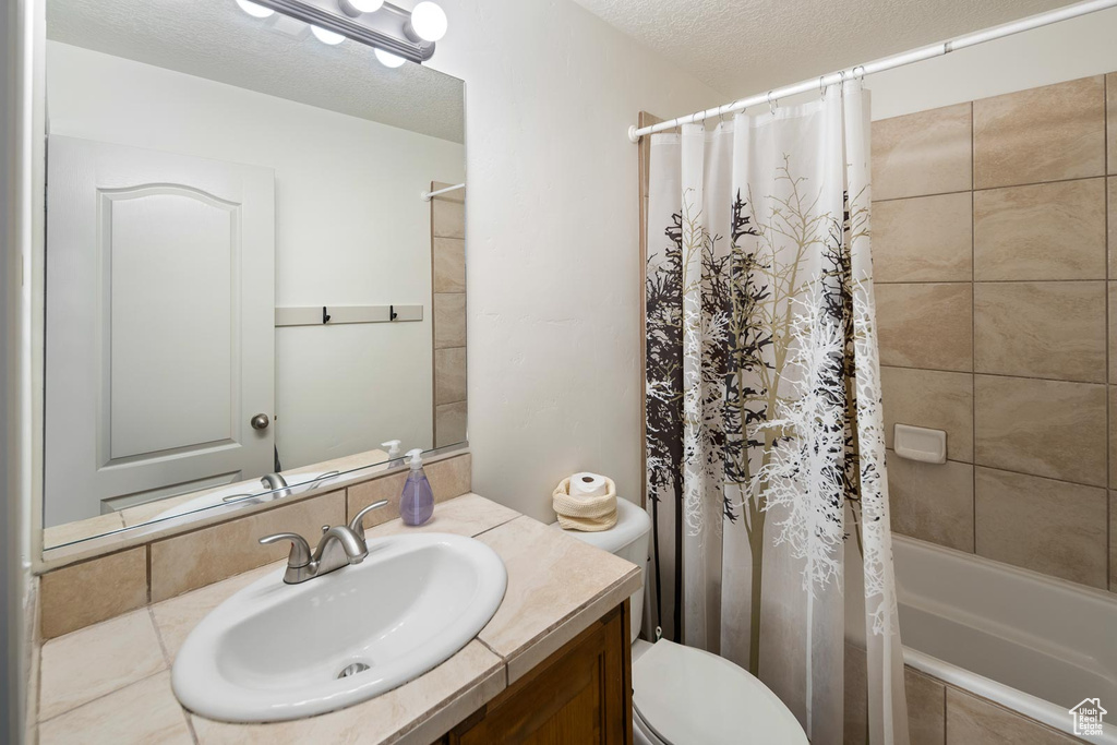 Full bathroom featuring a textured ceiling, toilet, shower / bathtub combination with curtain, and vanity