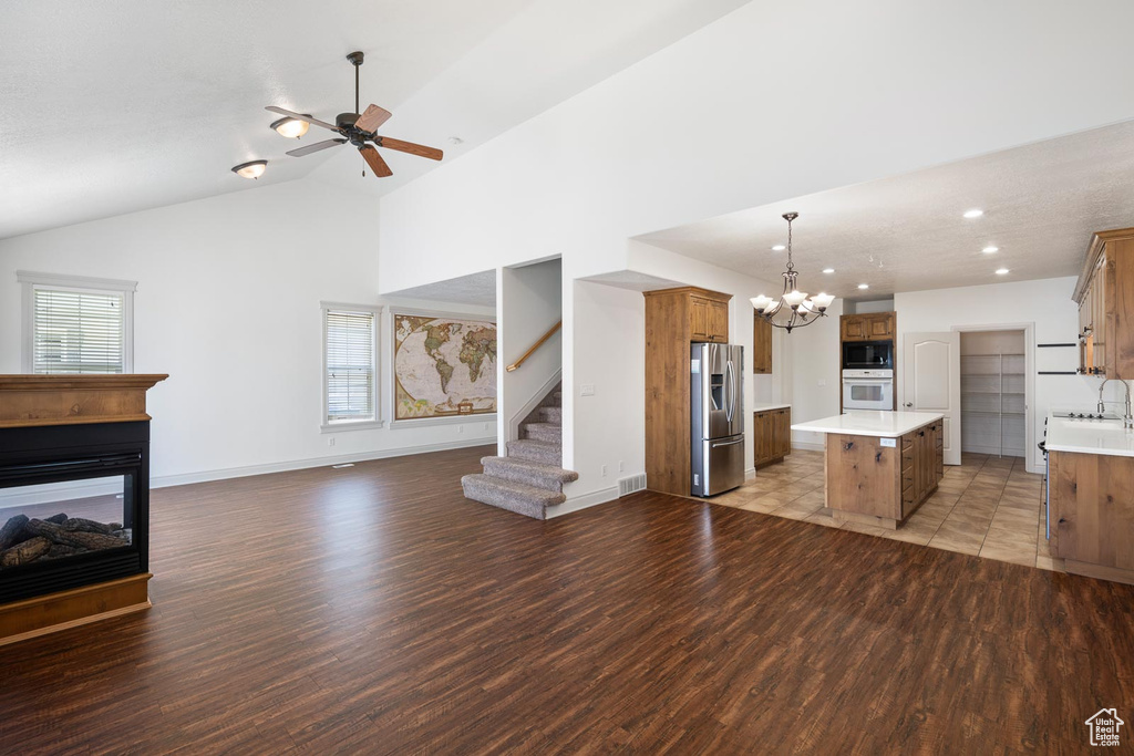 Unfurnished living room featuring a multi sided fireplace, ceiling fan with notable chandelier, light hardwood / wood-style floors, and a healthy amount of sunlight