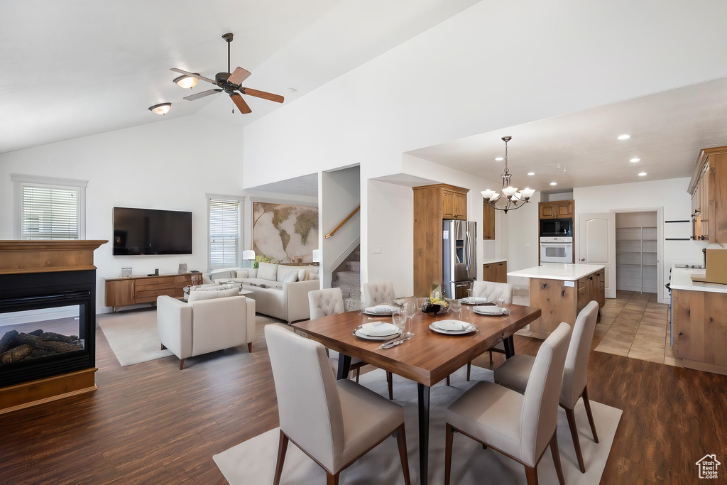 Dining area with high vaulted ceiling, a multi sided fireplace, ceiling fan with notable chandelier, and hardwood / wood-style floors