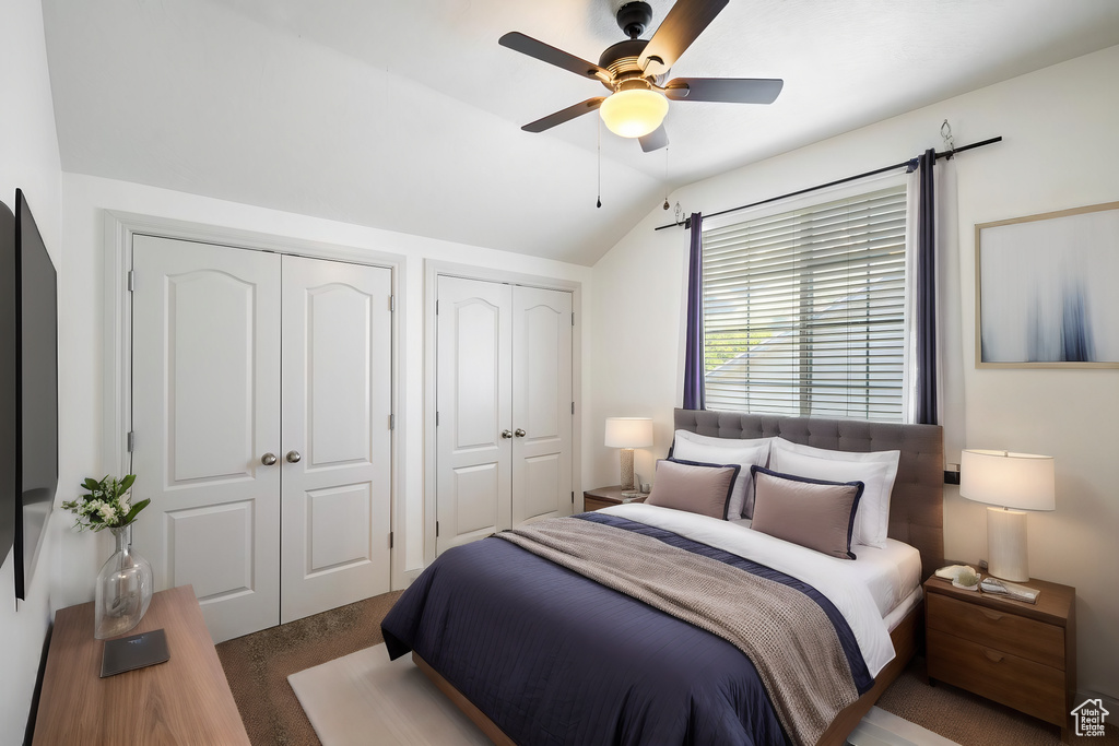 Bedroom with two closets, ceiling fan, lofted ceiling, and carpet flooring