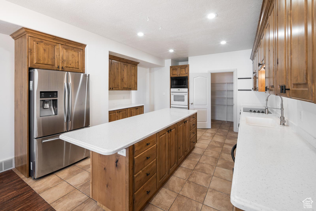 Kitchen featuring white oven, black microwave, stainless steel fridge, a kitchen island, and light tile floors