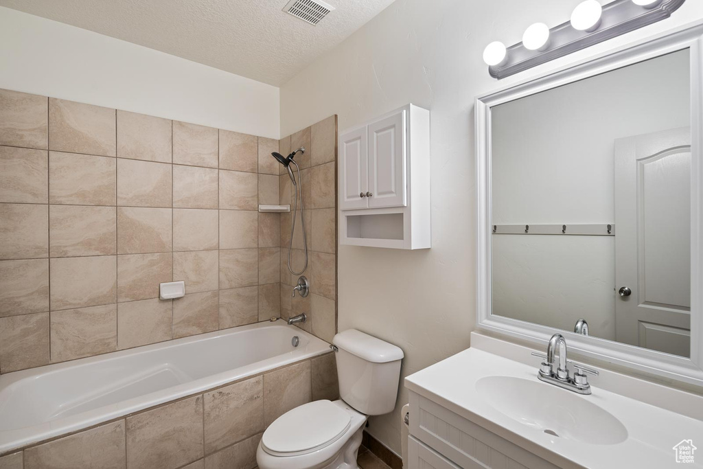 Full bathroom featuring a textured ceiling, vanity, toilet, and tiled shower / bath combo