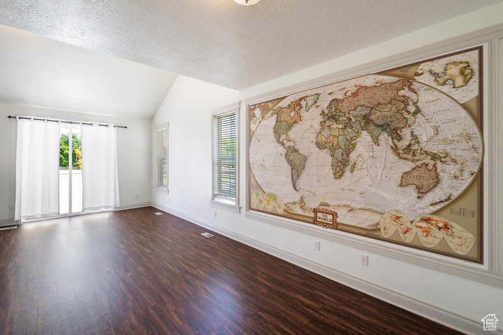 Unfurnished room featuring a healthy amount of sunlight, dark hardwood / wood-style flooring, a textured ceiling, and lofted ceiling