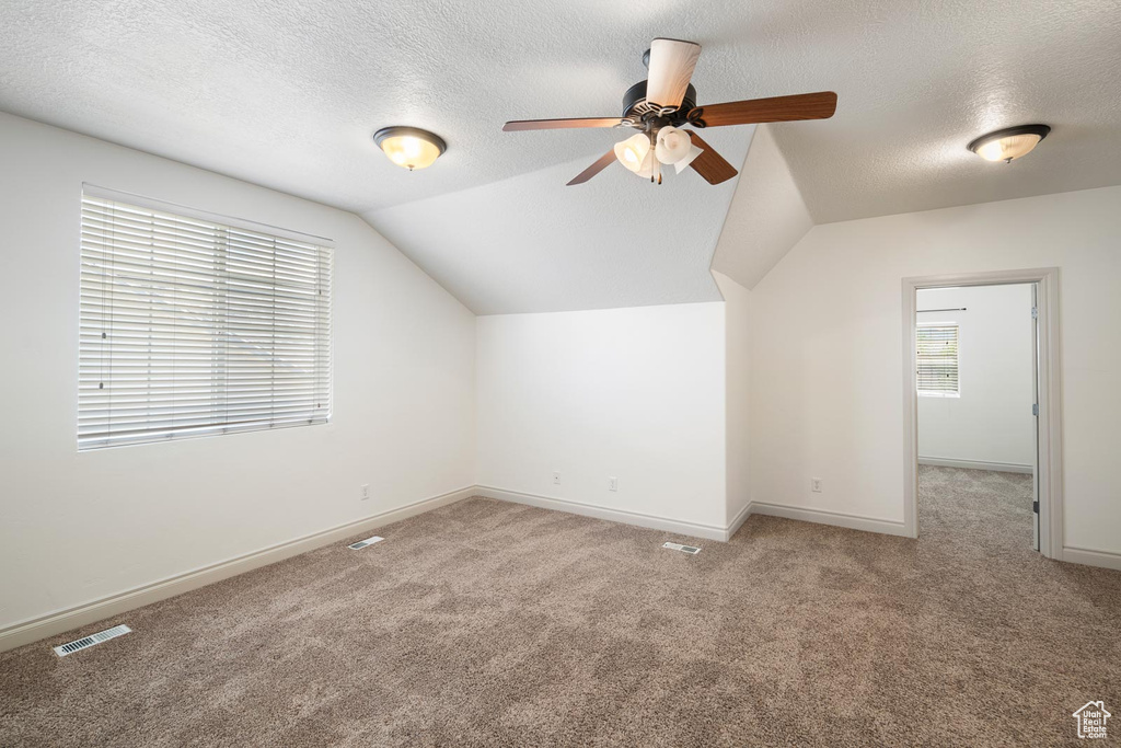 Additional living space with ceiling fan, vaulted ceiling, a textured ceiling, and carpet flooring