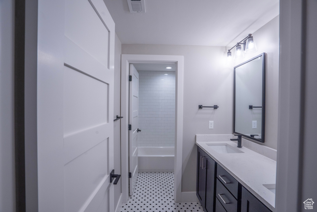 Bathroom with tile floors, dual sinks, vanity with extensive cabinet space, and tiled shower / bath