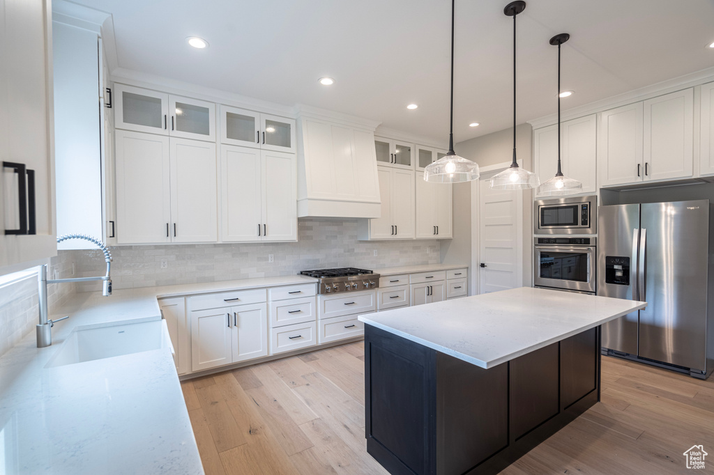 Kitchen featuring light wood-type flooring, custom range hood, stainless steel appliances, white cabinets, and tasteful backsplash