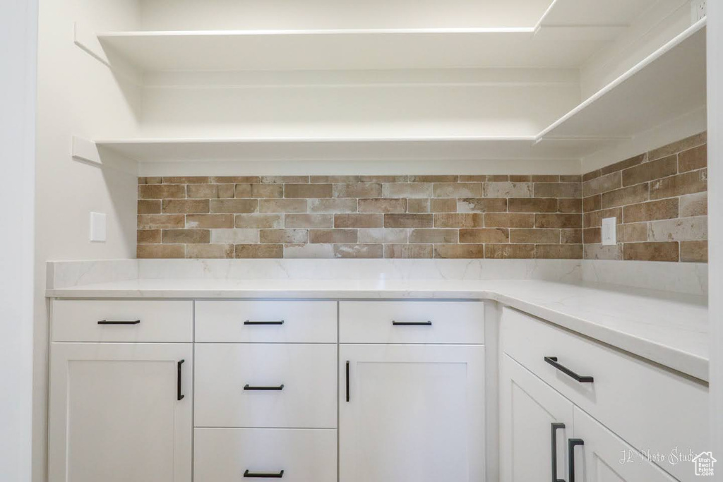 Interior space with white cabinets, tasteful backsplash, and light stone countertops