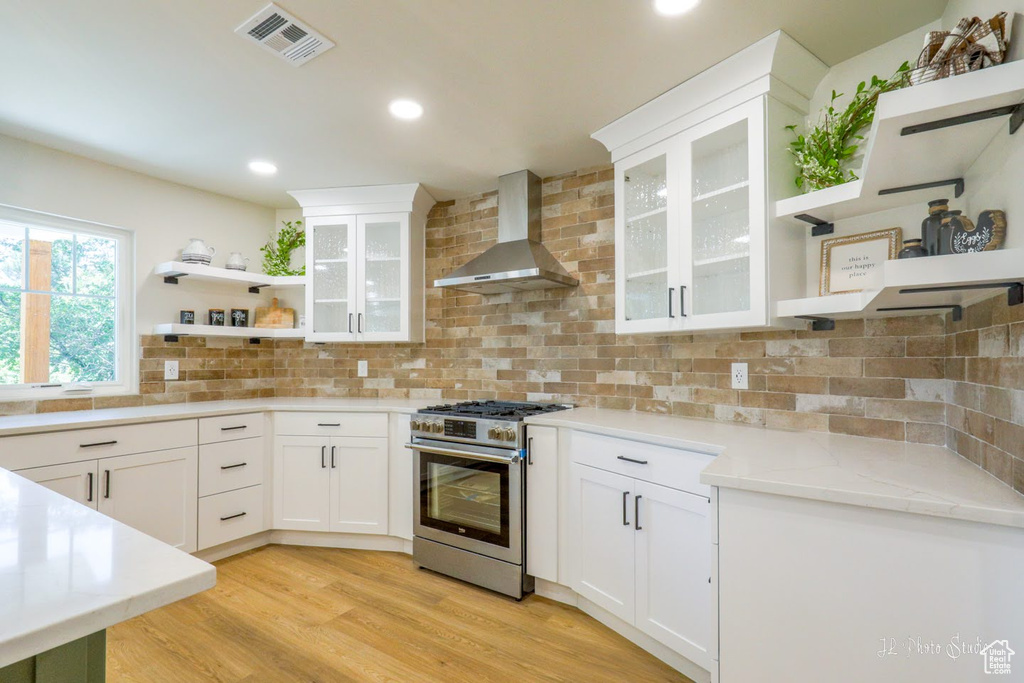 Kitchen with backsplash, wall chimney exhaust hood, light hardwood / wood-style floors, and stainless steel range with gas stovetop