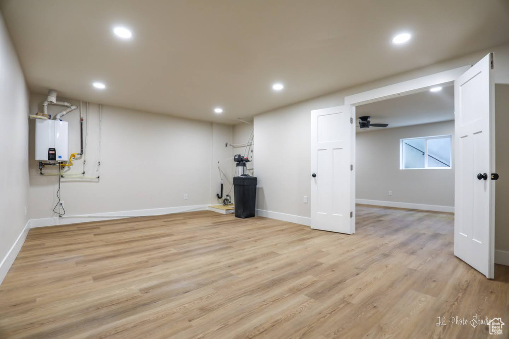 Basement featuring water heater, light wood-type flooring, and ceiling fan