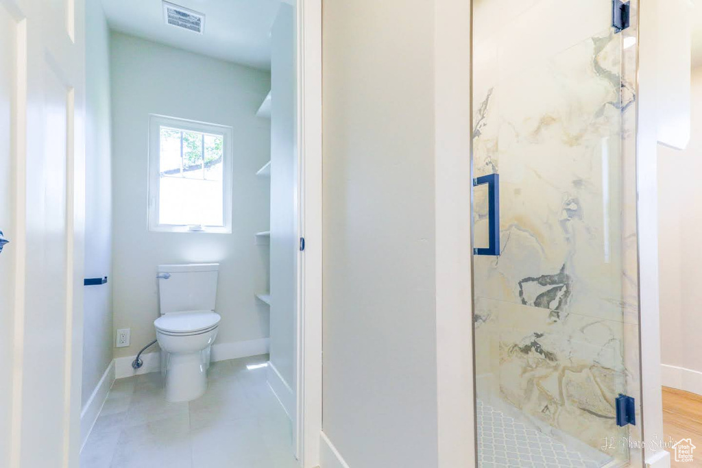 Bathroom with a tile shower, tile flooring, and toilet