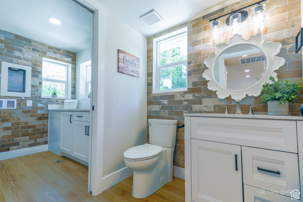 Bathroom featuring brick wall, vanity, toilet, and hardwood / wood-style flooring