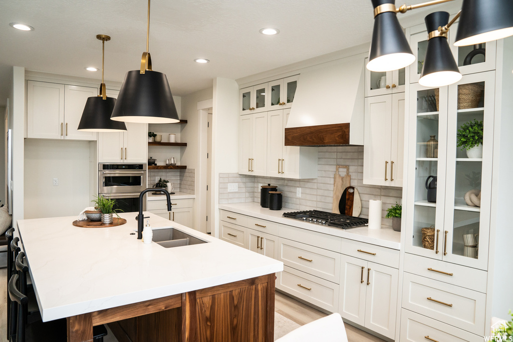 Kitchen featuring custom range hood, a center island with sink, tasteful backsplash, white cabinets, and sink